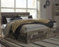 Cama Derekson tamaño King con cabecero y cuatro cajones, tocador con espejo, cómoda y mesita de noche.
