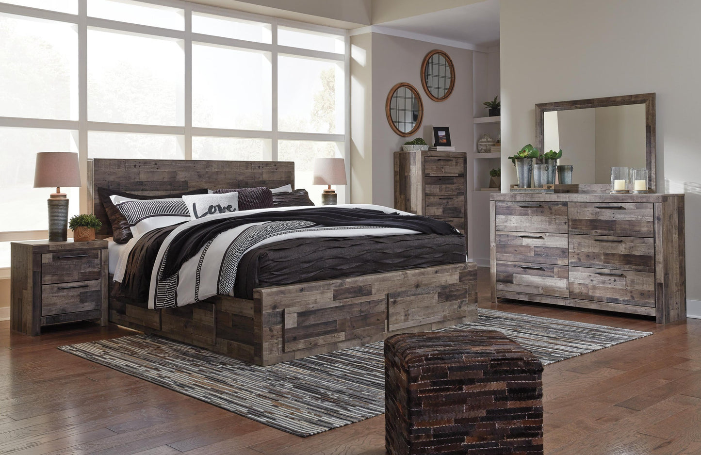Cama Derekson tamaño King con cabecero y cuatro cajones, tocador con espejo, cómoda y mesita de noche.